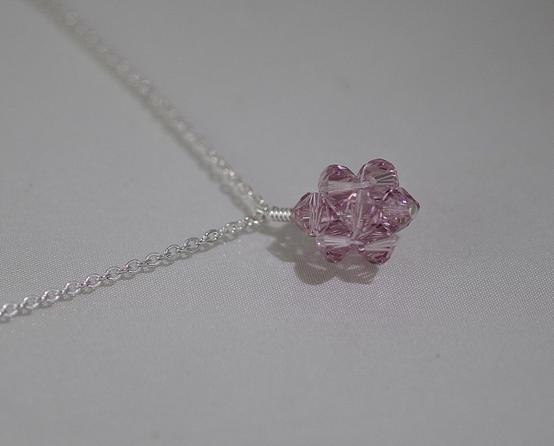 Puede incluir: Un delicado collar de cadena de plata con un colgante de cristal rosa. El colgante es un racimo de cristales facetados, creando un efecto brillante.