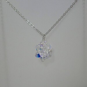 May include: A silver chain necklace with a clear crystal pendant. The pendant is made of many small crystals that are arranged in a geometric shape.
