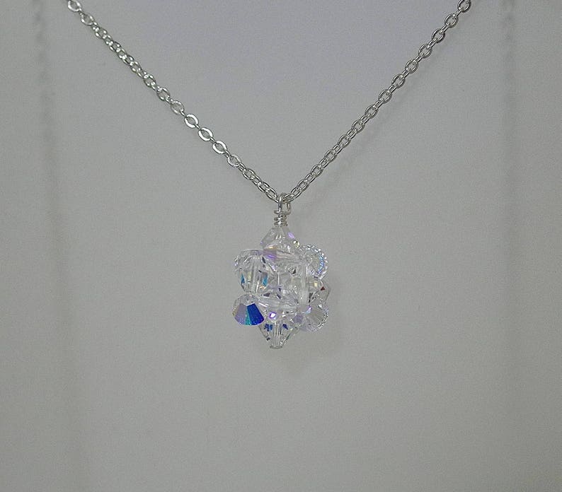 May include: A silver chain necklace with a clear crystal pendant. The pendant is made of many small crystals that are arranged in a geometric shape.