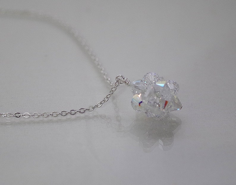Puede incluir: Un collar de cadena de plata con un colgante de cristal transparente. El colgante est&aacute; hecho de muchos cristales peque&ntilde;os que se agrupan para formar una bola.