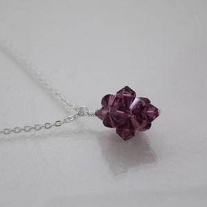 May include: A silver chain necklace with a purple crystal pendant. The pendant is a cluster of faceted crystals in a starburst shape.
