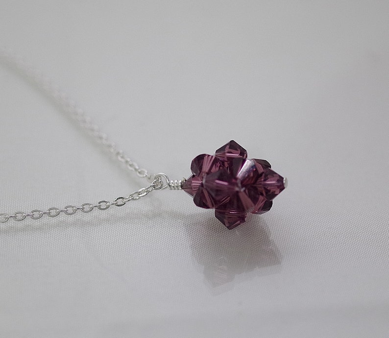 May include: A silver chain necklace with a purple crystal pendant. The pendant is a cluster of faceted crystals in a starburst shape.