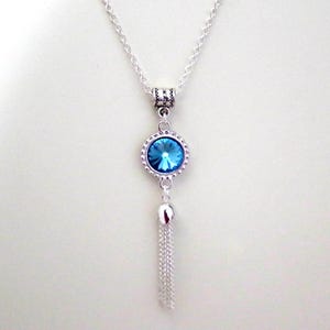 May include: A silver chain necklace with a blue crystal pendant and a silver tassel.