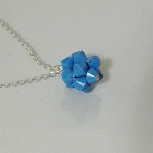 Puede incluir: Un collar de cadena de plata con un colgante de cristal azul. El colgante est&aacute; hecho de muchos cristales peque&ntilde;os y facetados que se agrupan para formar una bola.