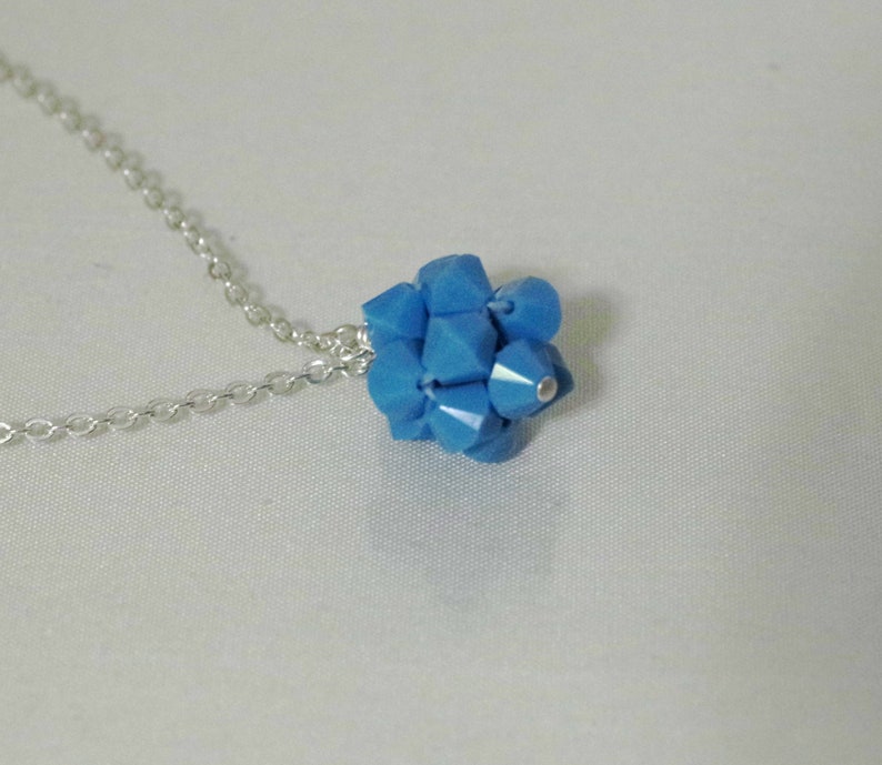 Puede incluir: Un collar de cadena de plata con un colgante de cristal azul. El colgante est&aacute; hecho de muchos cristales peque&ntilde;os y facetados que se agrupan para formar una bola.
