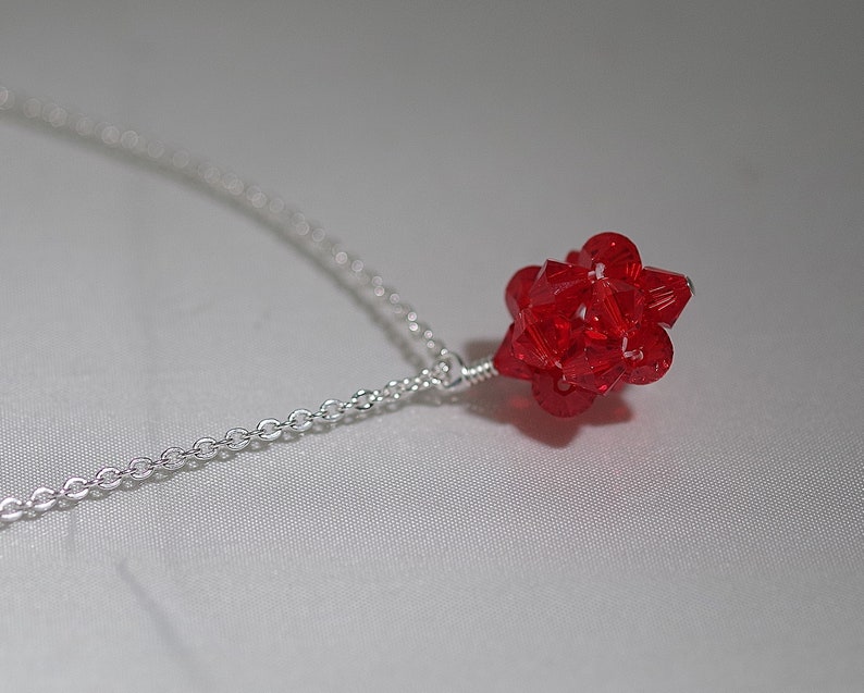 Puede incluir: Un collar de cadena de plata con un colgante de cristal rojo. El colgante es una forma geom&eacute;trica con muchas facetas.