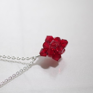 May include: A silver chain necklace with a red crystal pendant. The pendant is made of many small, faceted crystals that are clustered together to form a sphere.