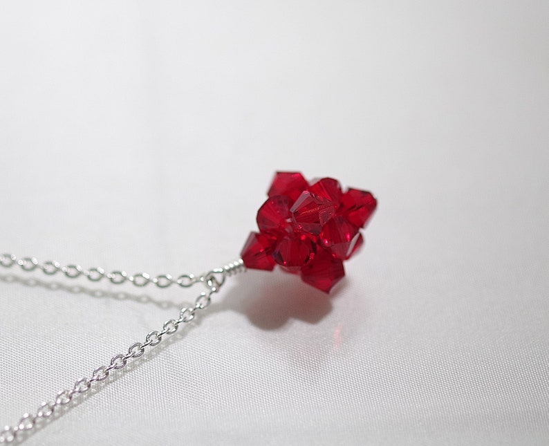 May include: A silver chain necklace with a red crystal pendant. The pendant is made of many small, faceted crystals that are clustered together to form a sphere.