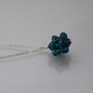 Puede incluir: Un collar de cadena de plata con un colgante de cristal azul oscuro. El colgante est&aacute; hecho de muchos cristales peque&ntilde;os que se agrupan para formar una bola.