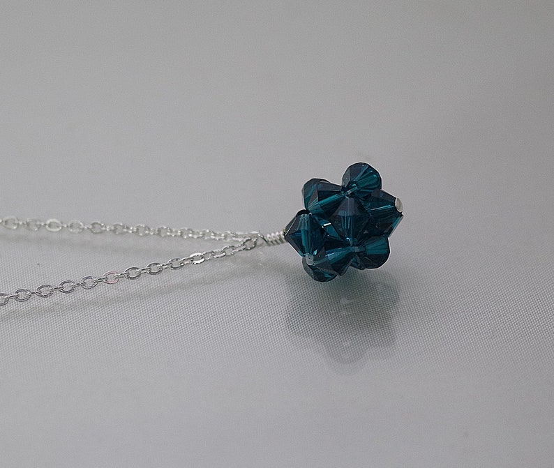 Puede incluir: Un collar de cadena de plata con un colgante de cristal azul oscuro. El colgante est&aacute; hecho de muchos cristales peque&ntilde;os que se agrupan para formar una bola.