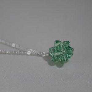 Puede incluir: Un collar de cadena de plata con un colgante de cristal verde. El colgante es una forma geom&eacute;trica con muchas facetas.