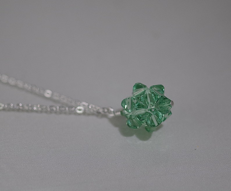 Puede incluir: Un collar de cadena de plata con un colgante de cristal verde. El colgante es una forma geom&eacute;trica con muchas facetas.