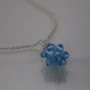 May include: A silver chain necklace with a light blue crystal pendant. The pendant is a cluster of small, faceted crystals.
