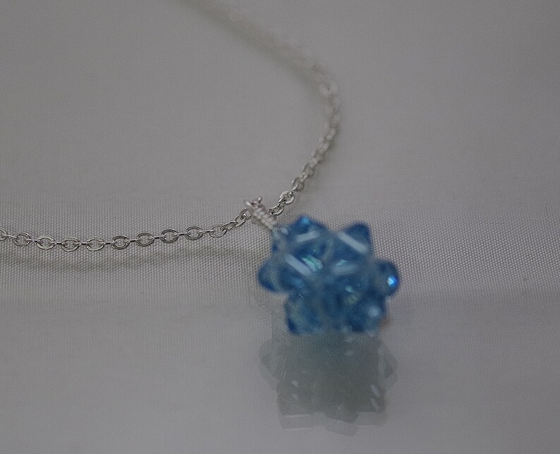 May include: A silver chain necklace with a light blue crystal pendant. The pendant is a cluster of small, faceted crystals.