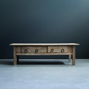 Op de afbeelding: Een rustieke houten salontafel met twee laden en metalen ringgrepen. De tafel is gemaakt van gerecycled hout en heeft een natuurlijke afwerking.
