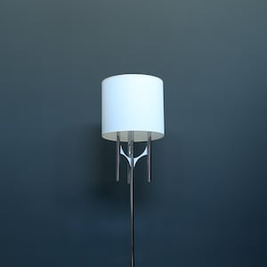 May include: A tall, modern floor lamp with a white cylindrical shade and a polished chrome base. The lamp features a sleek, minimalist design, perfect for contemporary home decor. The lamp's height is approximately 60 inches.
