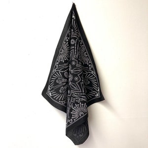 Puede incluir: Bandana negra con un dise&ntilde;o blanco de varias herramientas y s&iacute;mbolos. La bandana est&aacute; doblada y colgando de un gancho.