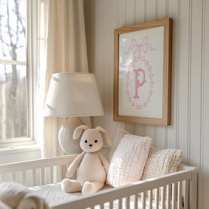 May include: A white crib with a white lamp, a stuffed bunny, and a framed print with a pink letter "P" and a bow.