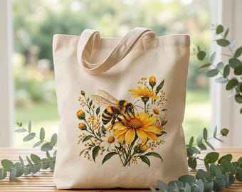 May include: A cream-coloured canvas tote bag featuring a central graphic illustration of a honeybee perched on a large yellow flower, surrounded by smaller yellow and white wildflowers, green stems, and buds, with two matching fabric handles.