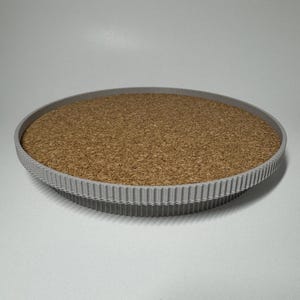 Könnte beinhalten: Ein rundes, graues, strukturiertes Tablett mit einem Kork-Einsatz. Das Tablett hat einen erhöhten, geriffelten Rand.