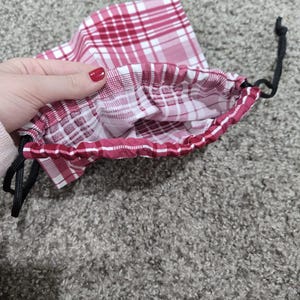 May include: A red and white plaid drawstring bag with a black drawstring. The bag is open and the inside is visible.