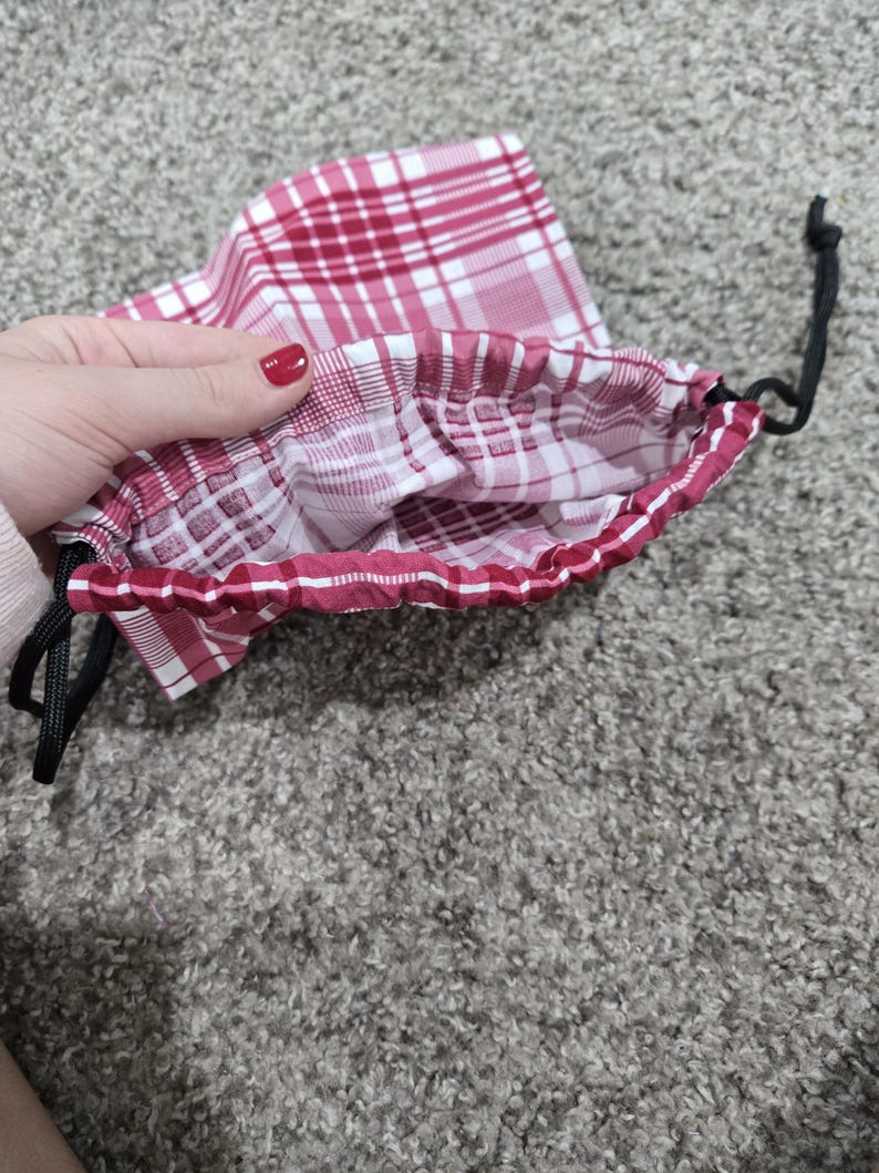 May include: A red and white plaid drawstring bag with a black drawstring. The bag is open and the inside is visible.