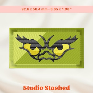 Op de afbeelding: Geborduurde patch met een gestileerd monstergezicht, gele ogen en zwarte details op een groene achtergrond. De patch meet 92,6 x 50,4 mm en heeft de tekst "Studio Stashed".