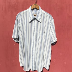 May include: Short-sleeved button-down shirt with vertical stripes in white and blue. The shirt has a collared neckline, a chest pocket, and is hanging on a wooden hanger.
