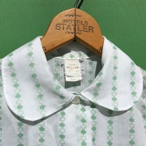 Puede incluir: Camisa blanca con cuello y estampado de tr&eacute;bol verde. La camisa tiene un cuello de Peter Pan y cierre de bot&oacute;n. La etiqueta dice "Official Irish School Size 12".