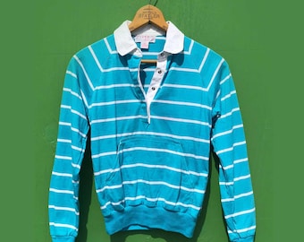 May include: A vintage turquoise and white striped long-sleeve shirt with a white collar and a front pocket. The shirt is hanging on a wooden hanger against a green background. The shirt has a button-up neckline.