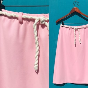 May include: A pink skirt with a white rope belt. The skirt is knee-length and has a simple, A-line silhouette.