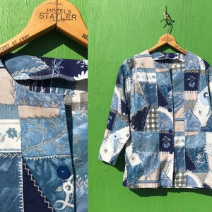 May include: A blue and white patchwork button-up shirt with a variety of floral and geometric patterns. The shirt has a collar and long sleeves.