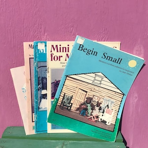 May include: A collection of four softcover instructional booklets for miniature furniture projects. The front book is light blue with the title Begin Small, featuring an illustration of a miniature house with bear figures and furniture patterns.