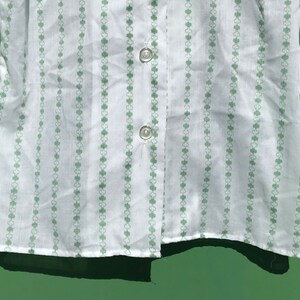 Puede incluir: Camisa blanca de botones con un patr&oacute;n de tr&eacute;bol verde.