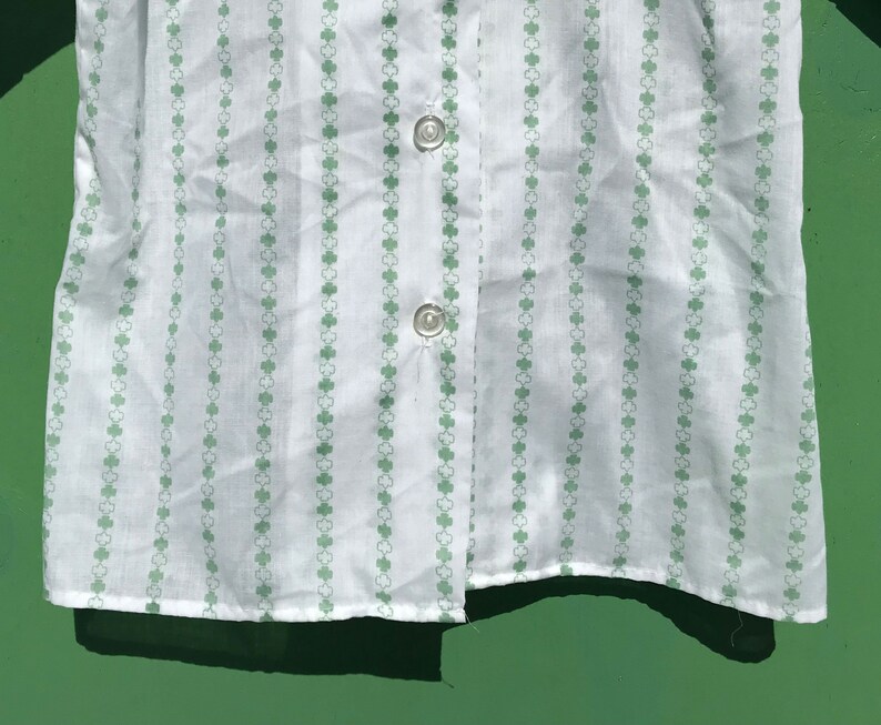 Puede incluir: Camisa blanca de botones con un patr&oacute;n de tr&eacute;bol verde.