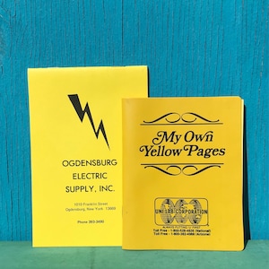 May include: Two yellow booklets. One features a black lightning bolt graphic and text for Ogdensburg Electric Supply, Inc. The other says "My Own Yellow Pages" with a Unilab Corporation logo. Both are on a blue wooden surface.