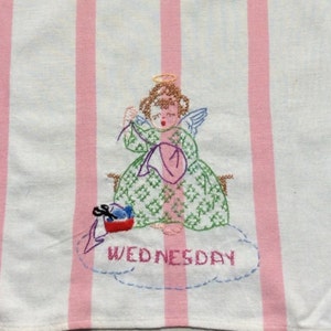 May include: White and pink striped tea towel featuring an embroidered angel design. The angel is wearing a green dress and holding a pink heart. The word "WEDNESDAY" is embroidered below the angel.