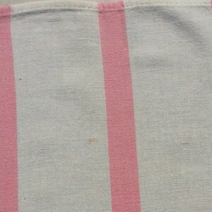 May include: Close-up of a white and pink striped fabric. The stripes are vertical and evenly spaced. The fabric appears to be a light, woven material, possibly cotton or linen. The pink stripes are a vibrant, solid colour.
