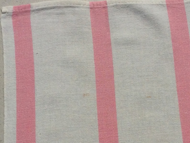 May include: Close-up of a white and pink striped fabric. The stripes are vertical and evenly spaced. The fabric appears to be a light, woven material, possibly cotton or linen. The pink stripes are a vibrant, solid colour.