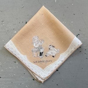 May include: A vintage tan handkerchief with a white scalloped border. The center features a black and white illustration of a girl and a doll, with the word "WEDNESDAY" below. The handkerchief has small black dots scattered across the fabric.