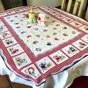 May include: White tablecloth with a red and blue checkered border. The tablecloth features a repeating pattern of teapots, cups, and saucers in a vintage style.