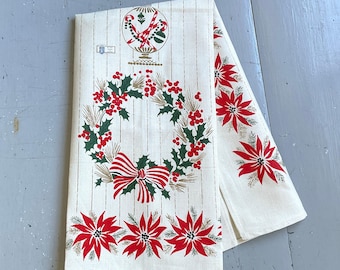 May include: Cream-colored Christmas-themed kitchen towel with a wreath of holly and berries, a red and white striped bow, and red poinsettias. The towel has vertical stripes and a decorative top design.