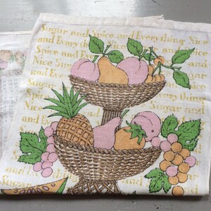 May include: A white tea towel with a vintage design featuring a two-tiered fruit basket filled with pears, peaches, grapes, and a pineapple. The text "Sugar and spice and everything nice" is printed on the towel.