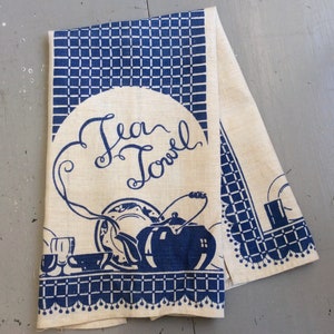 May include: A white tea towel with a blue and white checkered pattern. The towel has a blue graphic of a teapot, cups, and a plate with the text "Tea Towel" in a blue cursive font.