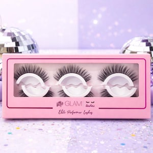 May include: A pink box of false eyelashes with the text "little GLAM lashes Elite Performer Lashes". The box contains three sets of black eyelashes. The background includes disco balls and purple spheres.