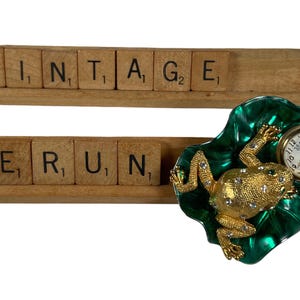 May include: Vintage spelled out with wooden letter tiles, and a gold frog figurine with a clock face on its back, sitting on a green leaf.