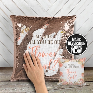 May include: A rose gold sequin pillow with the text "MADDIE, WILL YOU BE OUR FLOWER GIRL?" on one side and a floral pattern on the other side. The pillow is reversible and has a soft, plush feel.
