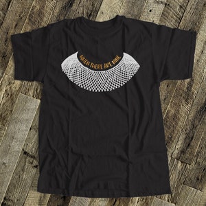 May include: Black t-shirt with a white outline of a collar and the text "When there are nine" in orange.