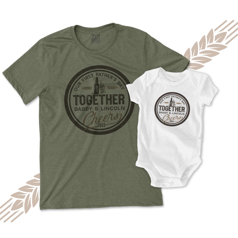 May include: A green t-shirt and a white onesie with a brown circle design that says "Our First Father's Day Together Daddy & Lincoln Cheers 2023".