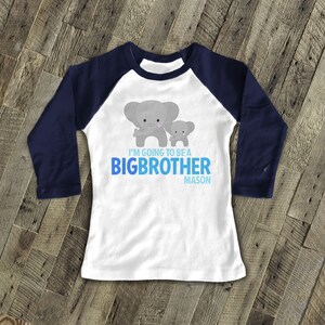 May include: White long-sleeved baseball tee with navy blue sleeves. The shirt features a grey elephant and a smaller grey elephant with the text "I'm going to be a big brother Mason".